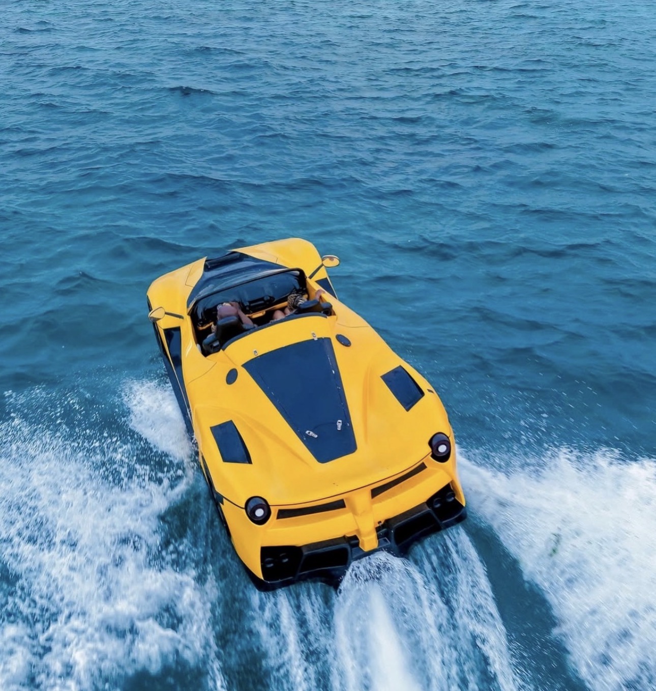 Aerial view of a yellow jetcar cutting across blue water